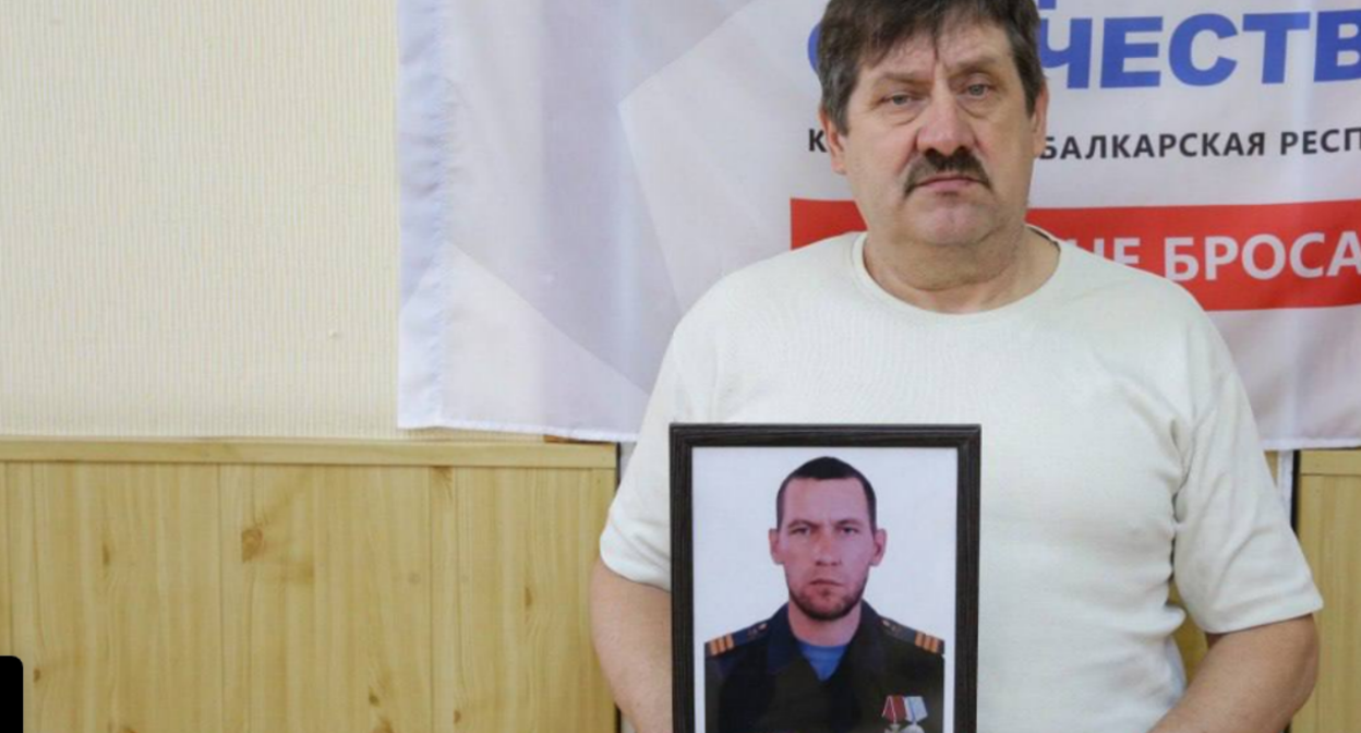 Отец Евгения Кадунова с его фотографией. Скриншот фото из Telegram-канала фонда "Защитники Отечества" по Кабардино-Балкарии от 15.08.25, https://t.me/fond_ZO_kbr/7221