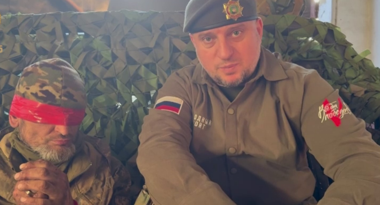 Украинский пленный с завязанными глазами и глава спецназа "Ахмат" Апти Алаудинов. Стоп-кадр видео из Telegram-канала Рамзана Кадырова от 20.04.25, https://t.me/RKadyrov_95/5668
