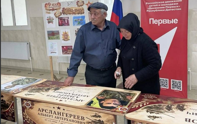 Родные на открытии именной парты. Скриншот фото администрации Бабаюртовского района от 25.05.26, https://t.me/babayurtrayon/12221?single Родные на открытии именной парты. Скриншот фото администрации Бабаюртовского района от 25.05.26, https://t.me/babayurtrayon/12221?single